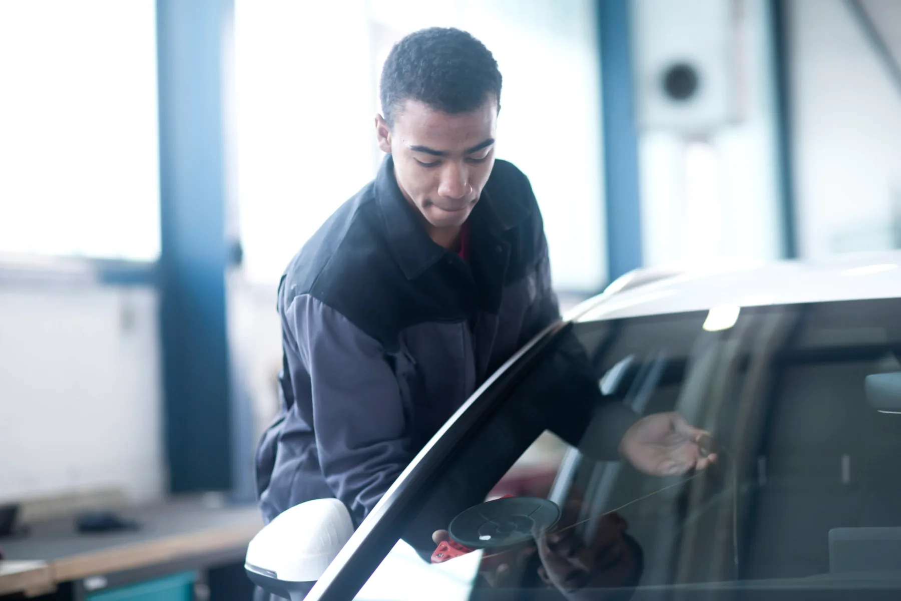 Auto glass technician holding a cracked windshield in a shop